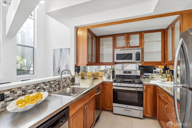 kitchen featuring tasteful backsplash, stainless steel counters, brown cabinets, appliances with stainless steel finishes, and a sink