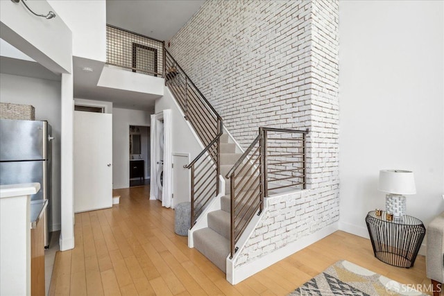 stairway featuring a high ceiling, wood finished floors, baseboards, and brick wall