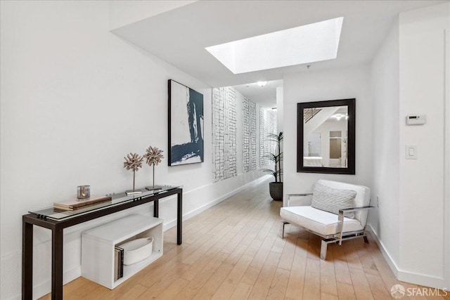 corridor featuring a skylight, light wood-style floors, and baseboards