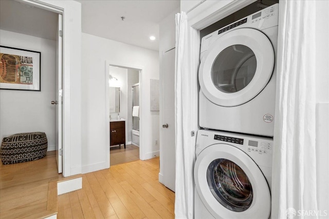 washroom featuring light wood finished floors, baseboards, laundry area, recessed lighting, and stacked washing maching and dryer