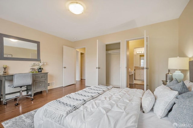 bedroom with wood finished floors, visible vents, and connected bathroom