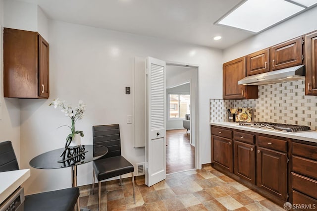 kitchen featuring under cabinet range hood, dishwashing machine, light countertops, decorative backsplash, and stainless steel gas cooktop