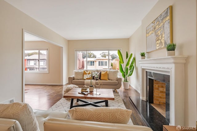 living room featuring visible vents, a healthy amount of sunlight, wood finished floors, and a high end fireplace