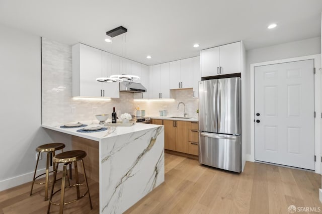 2055 42nd Ave, San Francisco, CA 94116 - kitchen with freestanding refrigerator, under cabinet range hood, a peninsula, light wood-style floors, and a breakfast bar