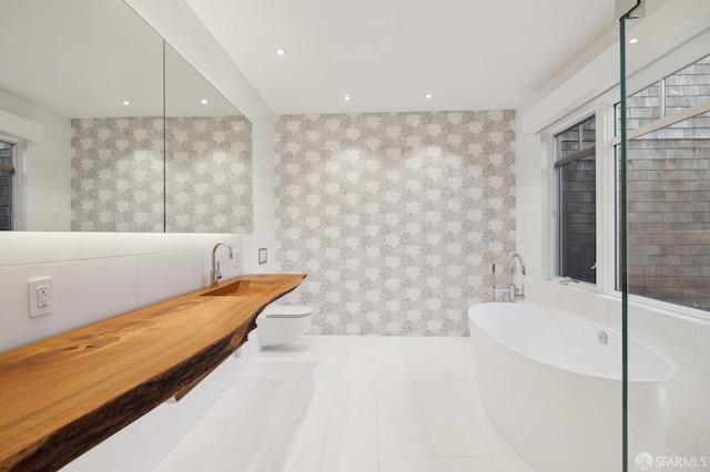 full bath with toilet, a soaking tub, a sink, tile walls, and recessed lighting