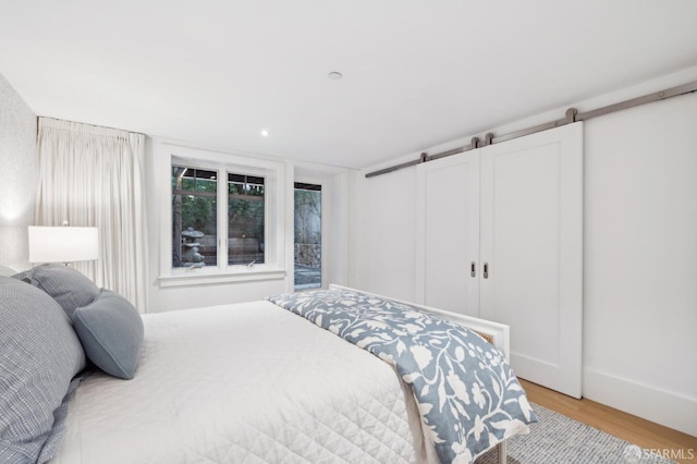 bedroom with light wood-style floors, baseboards, and a barn door