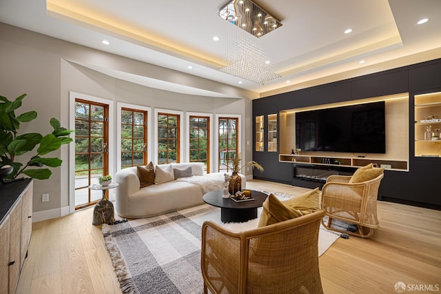living room with a tray ceiling, a chandelier, recessed lighting, light wood-type flooring, and baseboards