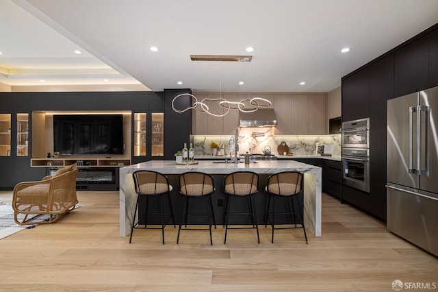 kitchen featuring stainless steel appliances, modern cabinets, wall chimney range hood, a kitchen breakfast bar, and decorative backsplash