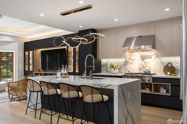 kitchen featuring modern cabinets, wall chimney range hood, a sink, light wood-style floors, and tasteful backsplash