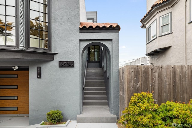 doorway to property featuring stucco siding, a tiled roof, and fence