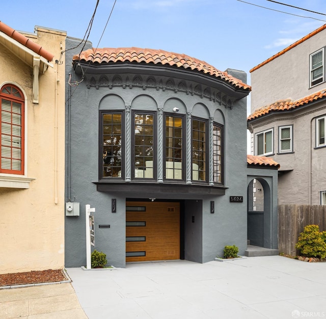 mediterranean / spanish home with concrete driveway, an attached garage, a tile roof, and stucco siding