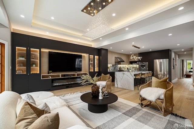 living room with a chandelier, light wood-type flooring, recessed lighting, and a raised ceiling