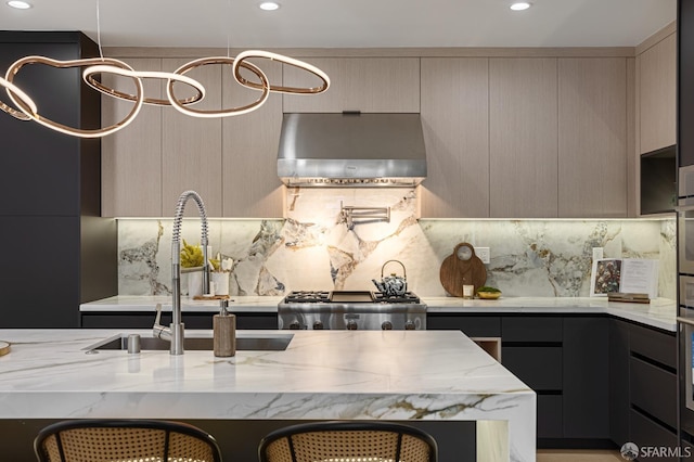 kitchen featuring wall chimney range hood, a sink, light stone counters, decorative backsplash, and modern cabinets