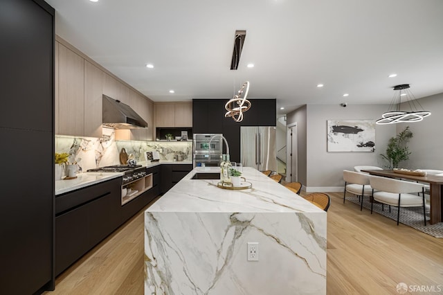 kitchen with stainless steel appliances, modern cabinets, under cabinet range hood, a sink, and a kitchen island with sink