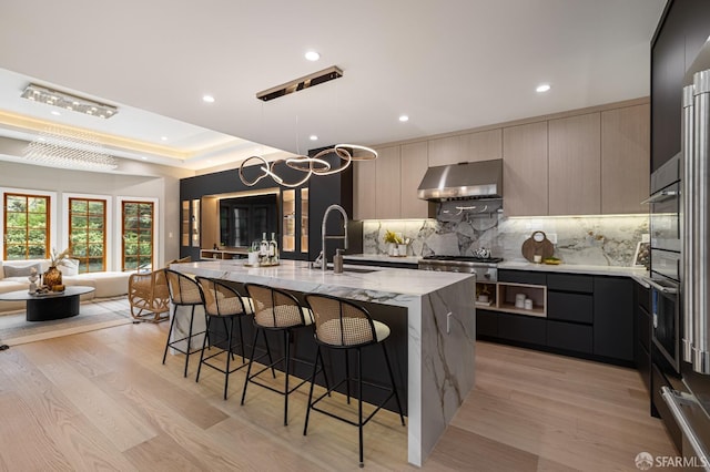 kitchen with modern cabinets, exhaust hood, a sink, backsplash, and recessed lighting
