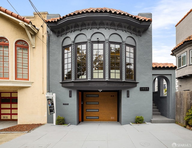 view of front of home with stucco siding, driveway, a tile roof, and a garage