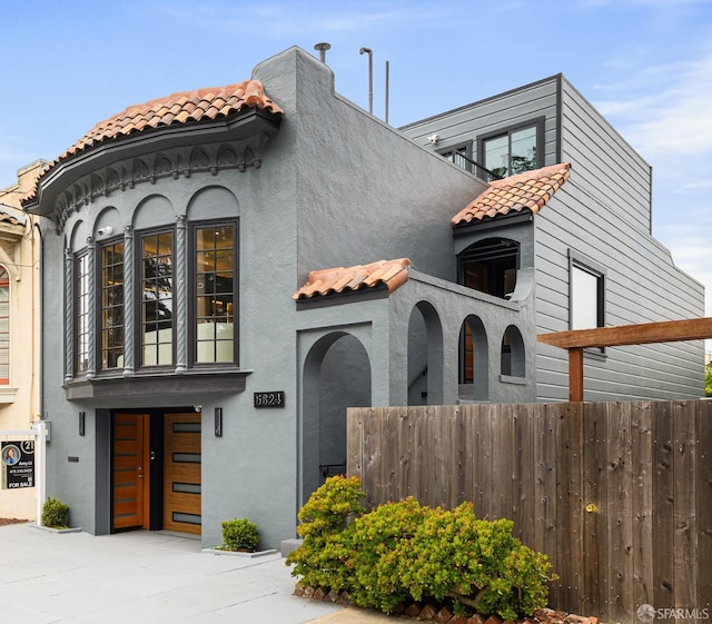 mediterranean / spanish-style home with stucco siding, a tile roof, and fence