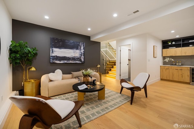 living area featuring bar with sink, stairway, light wood finished floors, baseboards, and recessed lighting