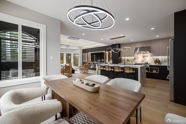dining area featuring a chandelier, recessed lighting, light wood-type flooring, and a tray ceiling