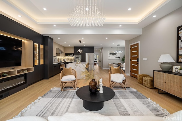 living area featuring a tray ceiling, a chandelier, light wood-style flooring, and recessed lighting