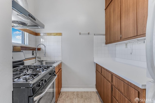 kitchen featuring a sink, light countertops, ventilation hood, brown cabinets, and gas stove