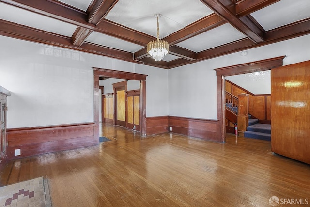 living room with a notable chandelier, wainscoting, wood finished floors, coffered ceiling, and stairs