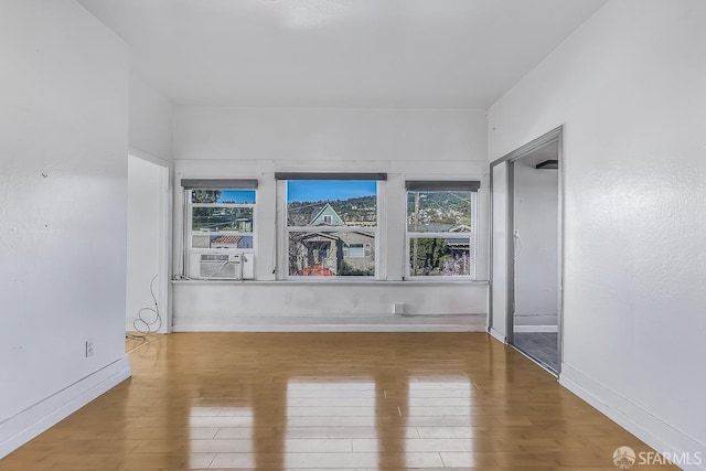 empty room featuring cooling unit, baseboards, and wood finished floors