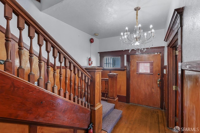 foyer with a textured ceiling, stairway, wood finished floors, and an inviting chandelier