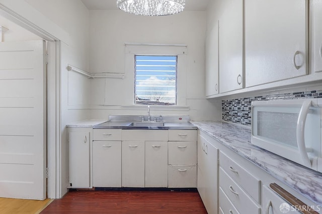 kitchen featuring white microwave, dark wood-type flooring, a sink, white cabinetry, and backsplash