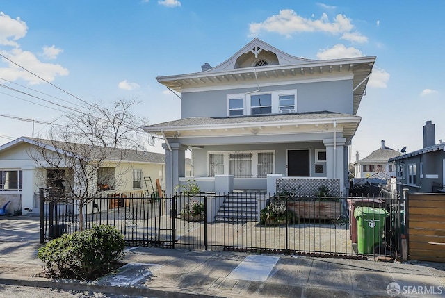 american foursquare style home featuring covered porch, a fenced front yard, and stucco siding