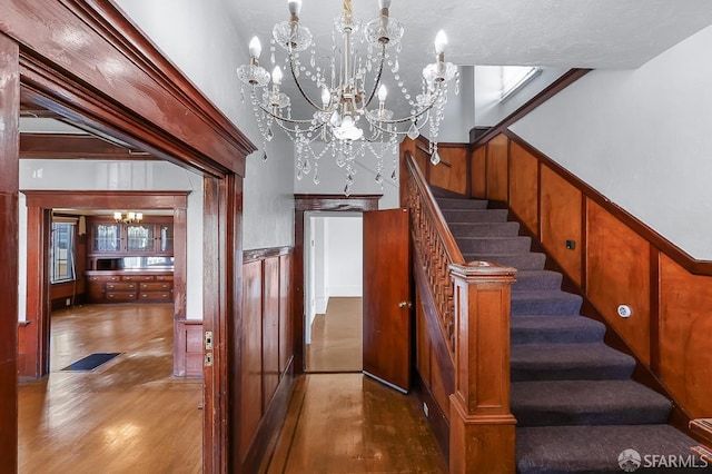 stairs with a notable chandelier, wooden walls, wood finished floors, and wainscoting