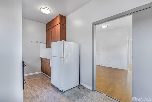 kitchen with light countertops, brown cabinetry, freestanding refrigerator, and baseboards