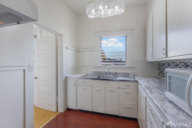 kitchen featuring tasteful backsplash, white microwave, dark wood-type flooring, white cabinetry, and a sink