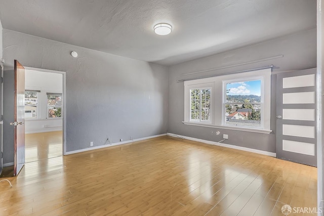 spare room with baseboards, a textured ceiling, and light wood-style floors