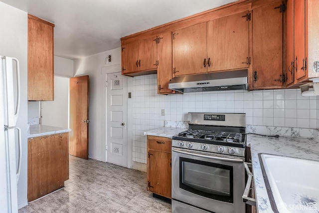 kitchen with gas range, brown cabinets, freestanding refrigerator, light countertops, and under cabinet range hood