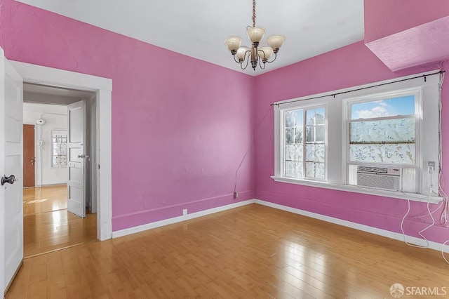 spare room featuring baseboards, a notable chandelier, and light wood finished floors