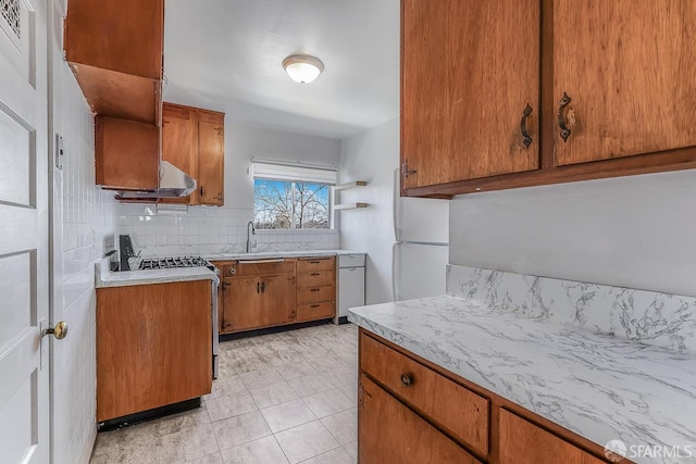 kitchen with brown cabinets, tasteful backsplash, light countertops, freestanding refrigerator, and gas range