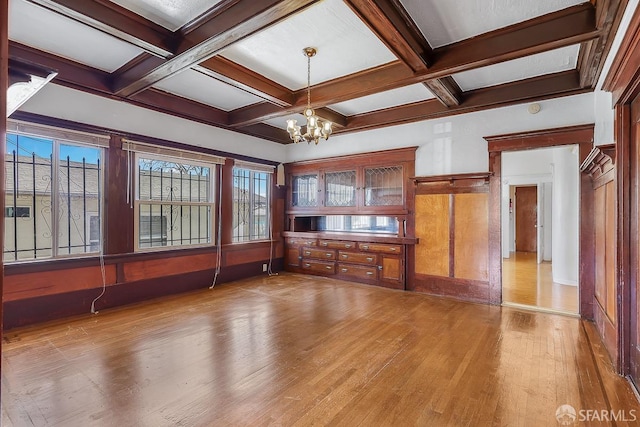 empty room with a notable chandelier, beam ceiling, coffered ceiling, and wood finished floors