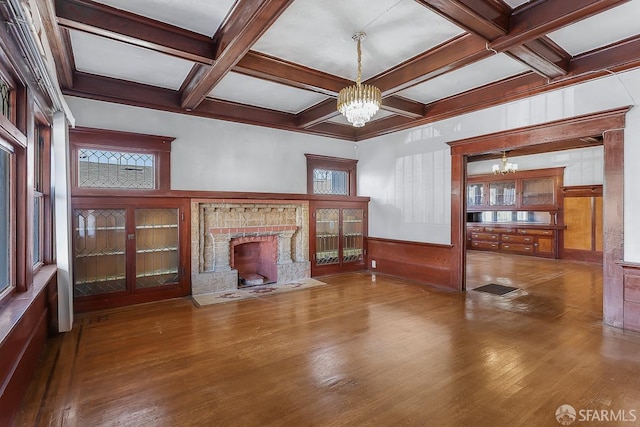 unfurnished living room with a stone fireplace, wood-type flooring, coffered ceiling, and a notable chandelier