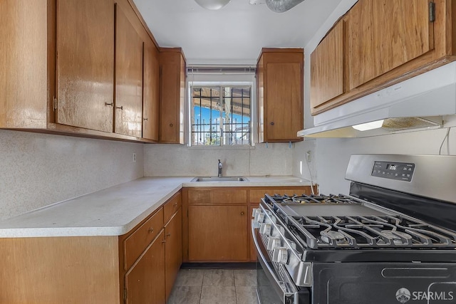 kitchen featuring brown cabinets, light countertops, a sink, stainless steel gas range, and under cabinet range hood