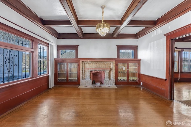 unfurnished living room featuring a fireplace with flush hearth, beam ceiling, a chandelier, and wood finished floors