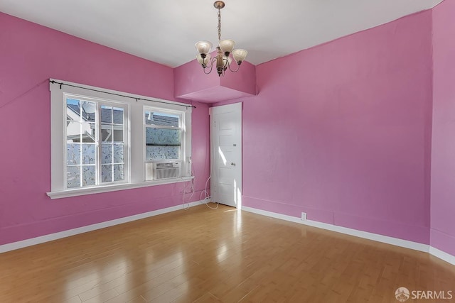 spare room featuring cooling unit, baseboards, an inviting chandelier, and wood finished floors