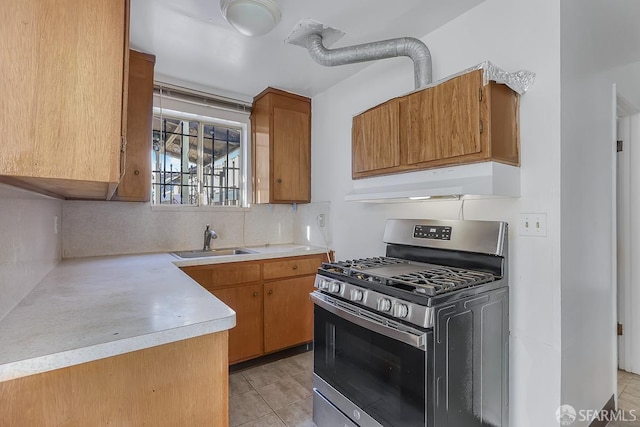 kitchen featuring stainless steel gas range, light countertops, under cabinet range hood, a sink, and light tile patterned flooring