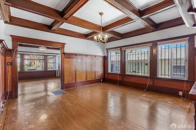 empty room featuring an inviting chandelier, wood-type flooring, coffered ceiling, and beam ceiling