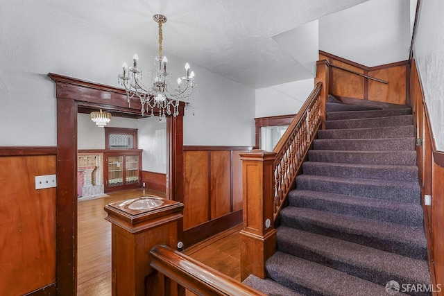 staircase featuring wooden walls, wainscoting, wood finished floors, and a notable chandelier