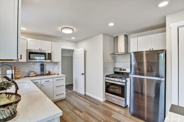 kitchen featuring tasteful backsplash, white cabinetry, wall chimney range hood, and appliances with stainless steel finishes