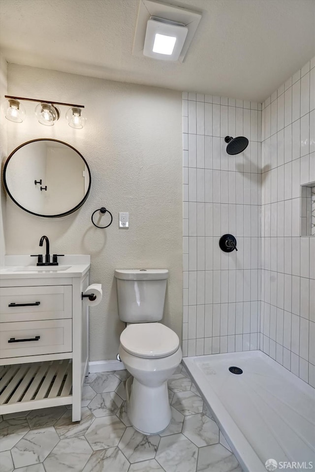 bathroom with a tile shower, vanity, and toilet