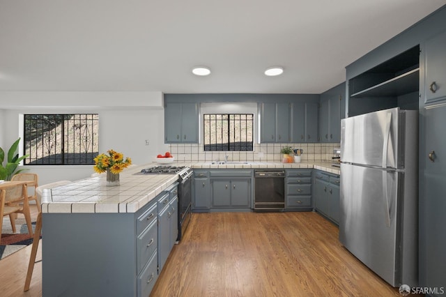 kitchen with wood finished floors, a peninsula, freestanding refrigerator, a sink, and tile counters