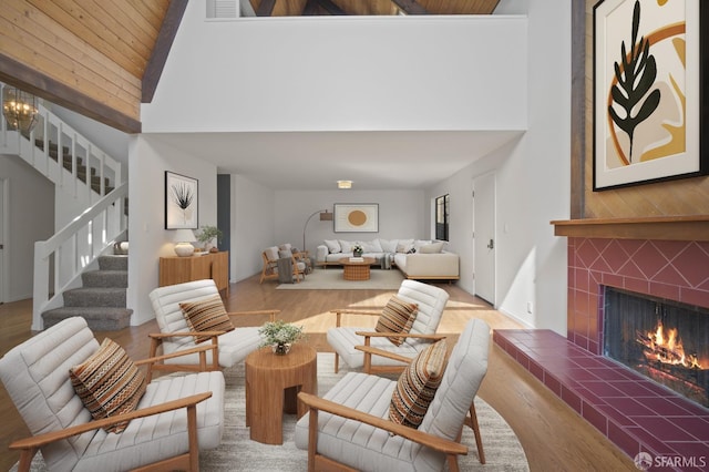 living area with stairway, a fireplace, high vaulted ceiling, and wood finished floors