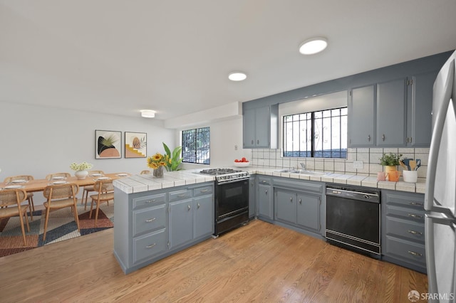 kitchen with light wood-style flooring, gray cabinets, black dishwasher, a peninsula, and gas range